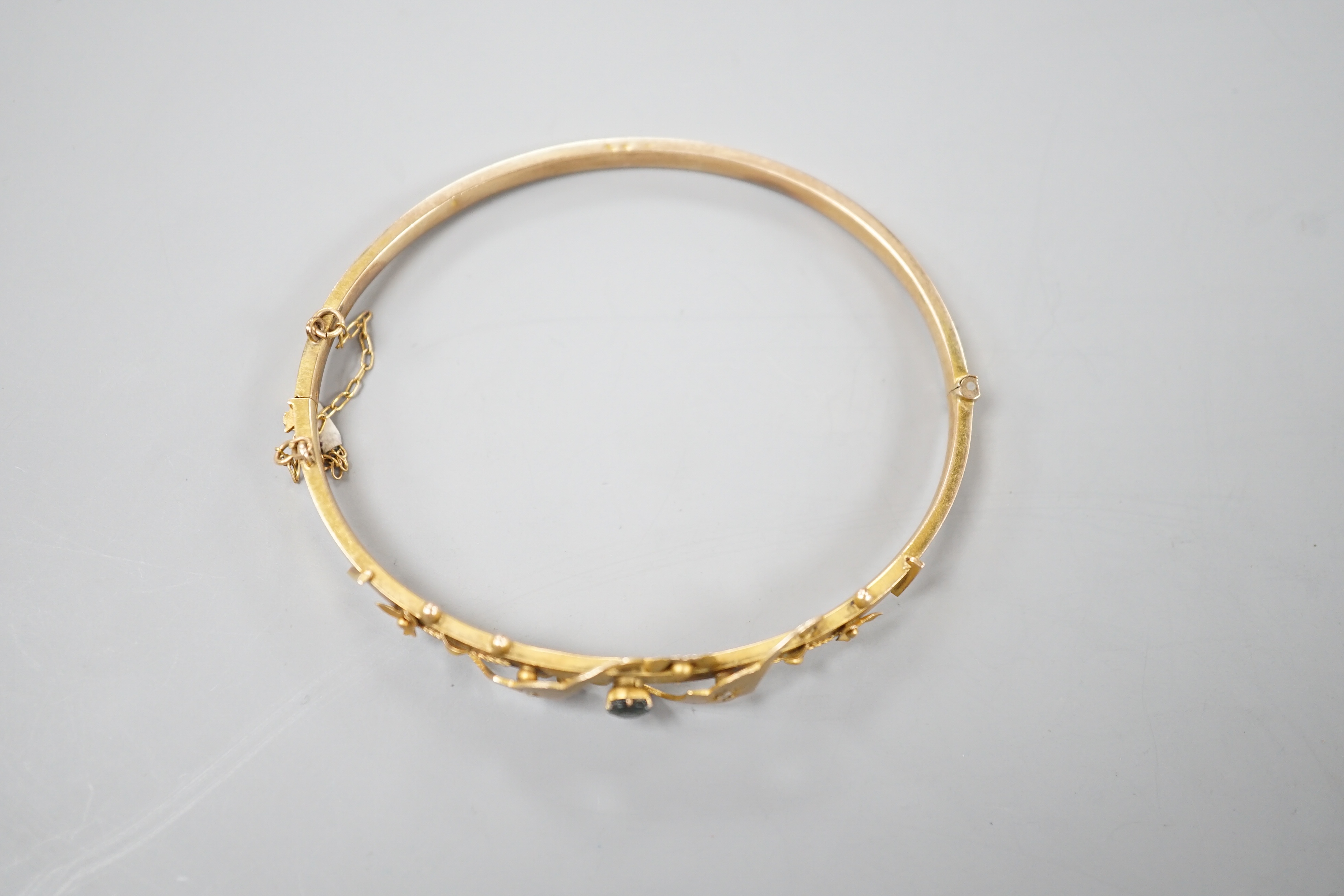 An early 20th century yellow metal, sapphire and diamond chip set hinged bangle, gross 5.4 grams.